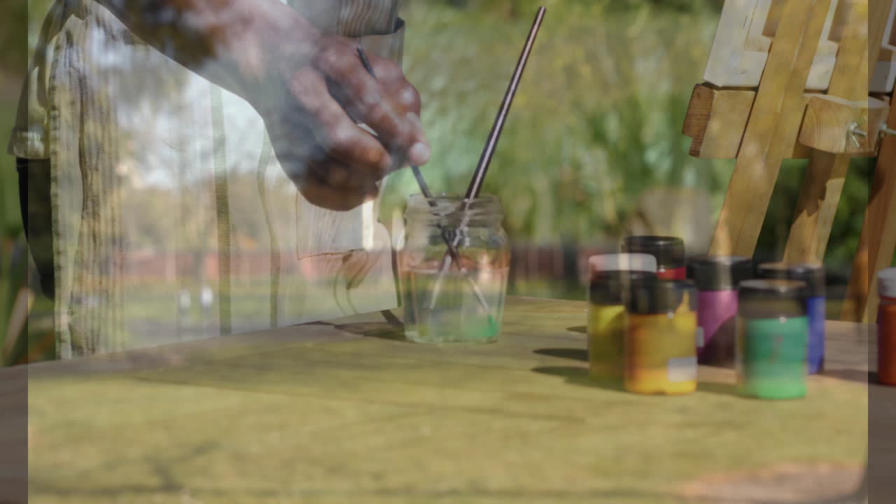 Tremper un pinceau dans un pot, mains se préparant pour l'animation sur une table d'extérieur