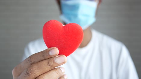 persona sosteniendo un corazón rojo con una máscara