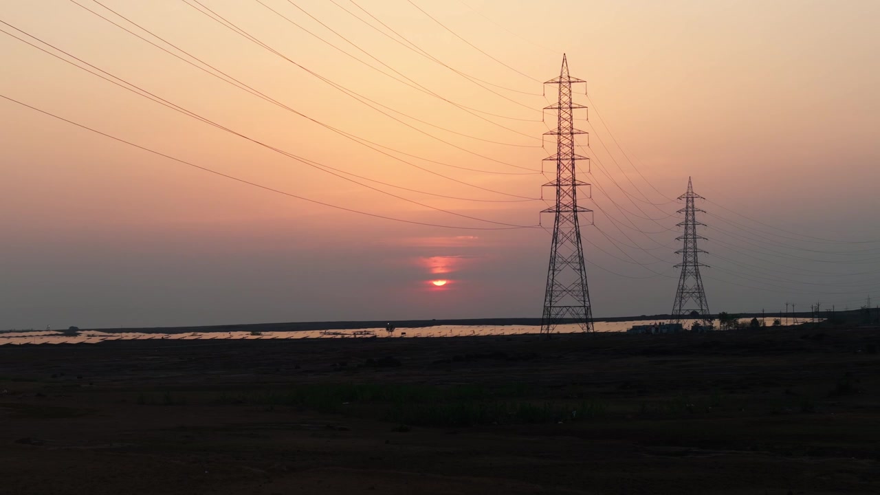 Drone descending over a photovoltaic solar farm with transmission towers, revealing renewable electricity, power infrastructure, and sustainable energy production.