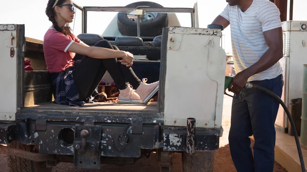 다양한 남성과 여성이 주유소에서 연료  ⁇ 프를 사용하여 트럭을 채우고 있습니다.
