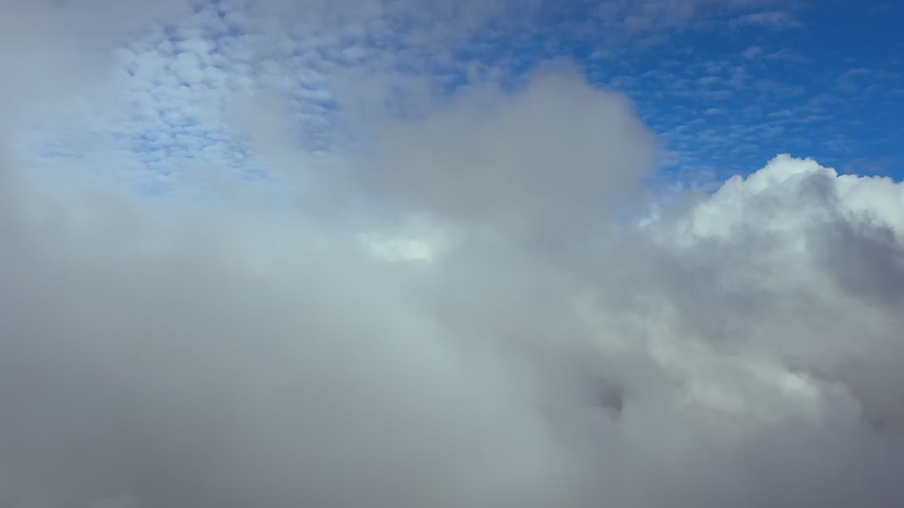 Perspectiva del piloto volando a través de un cielo turbulento lleno de nubes blancas y grises, y con nubes de tormenta por delante en un cielo azul