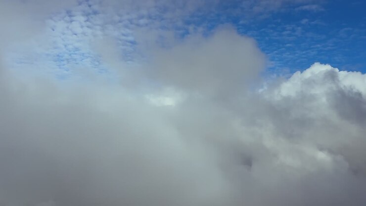 Pilot’s perspective flying through a turbulent sky full of white and grey clouds, and with storm clouds ahead in a blue sky