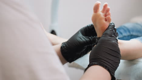 close-up view of technician wearing black gloves massaging underside of client foot and technician body is partially visible with focus on hands and foot, background softly blurred