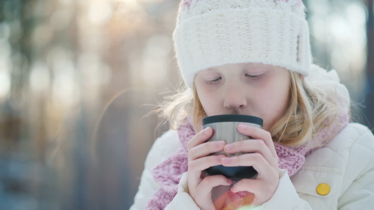Una ragazza beve tè caldo all'aperto sullo sfondo della foresta invernale.