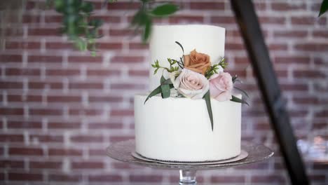 Elegante-Zweistöckige-Weiße-Hochzeitstorte-Auf-Glasständer-Mit-Floralem-Dekor