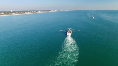 a white trawling shrimp boat on the water, aerial reverse flyover
