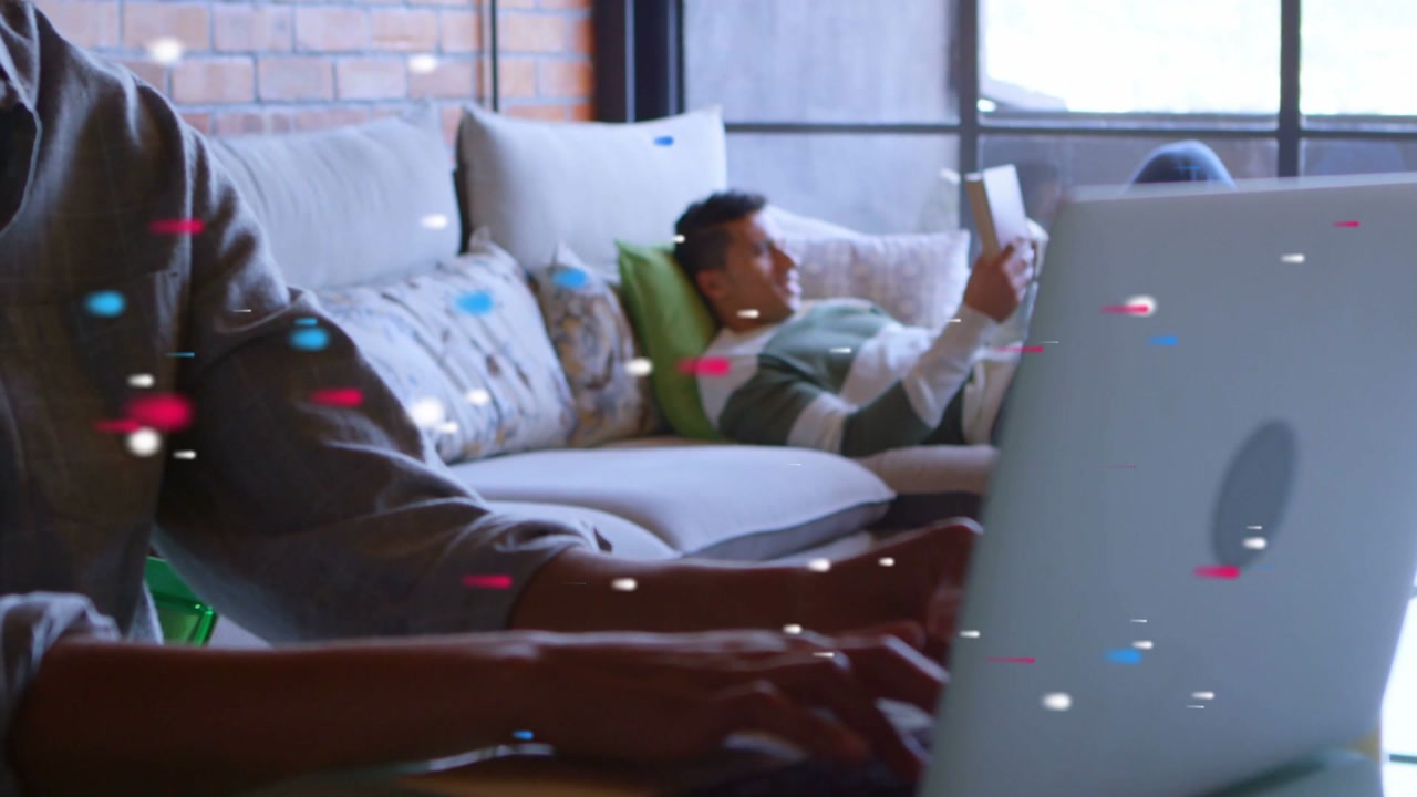 Man typing laptop at table starting remote work, woman reclining reading tablet, particles drifting