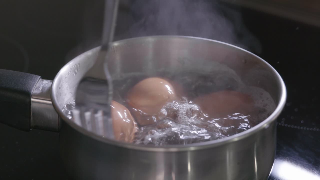 Three eggs boiling in a saucepan on an induction hob
