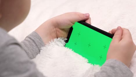 kid preschool with gadget watching video on mobile phone at home. child using and holding a smartphone green screen in hand, technology generation concept. focus on chromakey of the mobile phone