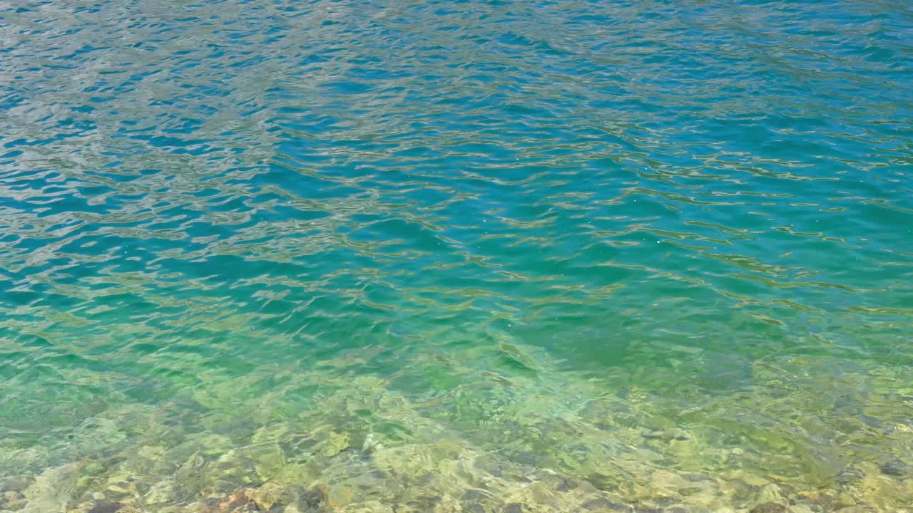 Top-down 4K shot of vibrant turquoise-green sea water rippling in sunlight. Sparkling surface forms an abstract natural background perfect for travel, nature or wellness projects