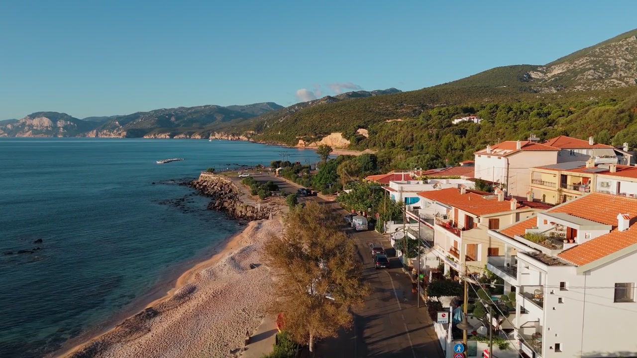 Cala Gonone, Sardegna, Italia, che mostra una città balneare, il Mar Mediterraneo, edifici sul lungomare e paesaggi montani lungo il Golfo di Orosei, carrellata aerea in avanti