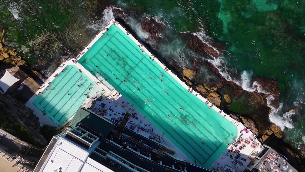 Downward drone footage of the ocean pool at Bondi Beach, Australia, with waves gently rolling on the shore. Ascending aerial footage.