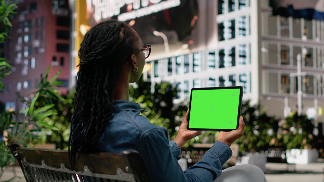 Chroma key skærm på tablet holdt af afroamerikansk pige siddende på en bænk