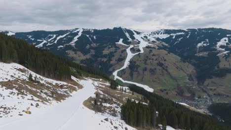 Bergige-Winterlandschaft-Mit-Schneeflecken-Im-Skigebiet-Saalbach-Hinterglemm,-Luftaufnahme