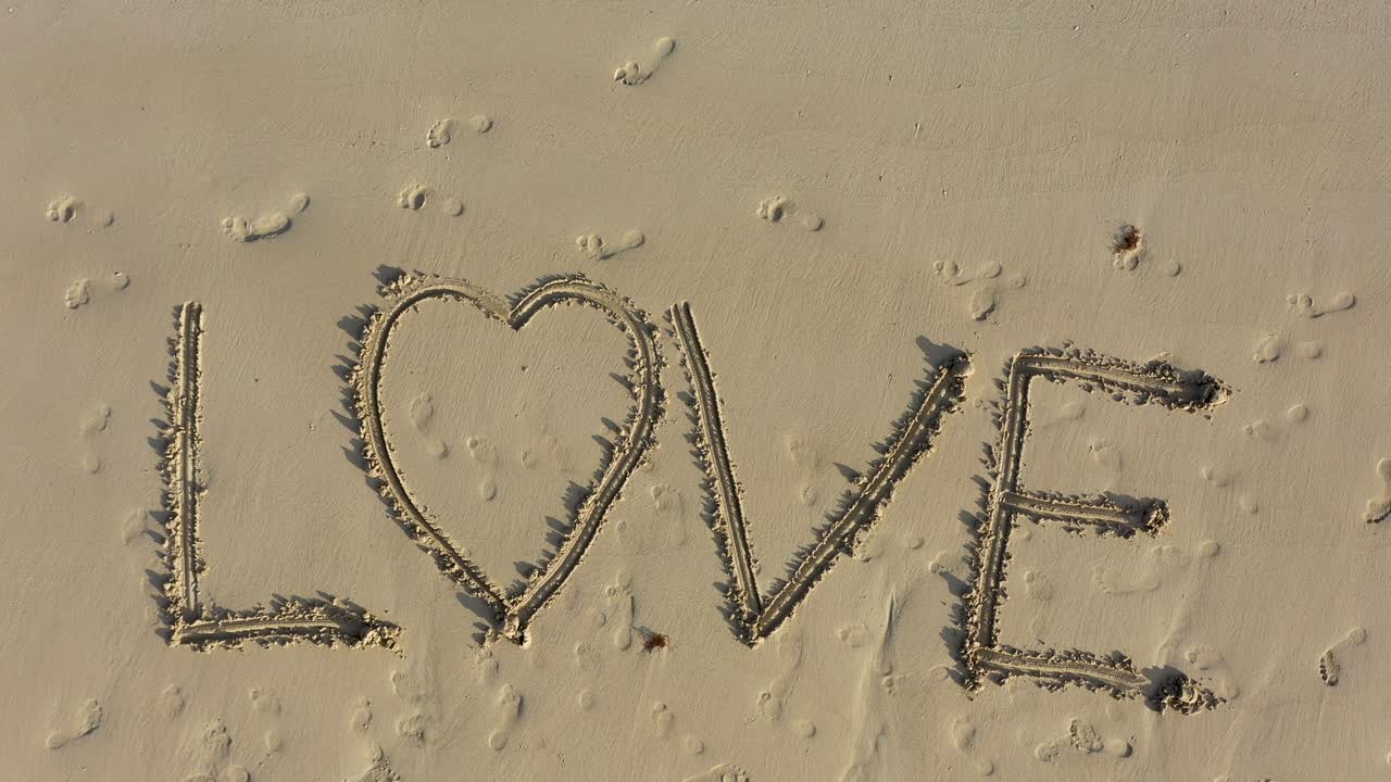 해변의 모래에 새겨진 사랑을 향해 내려가는 항공 카메라