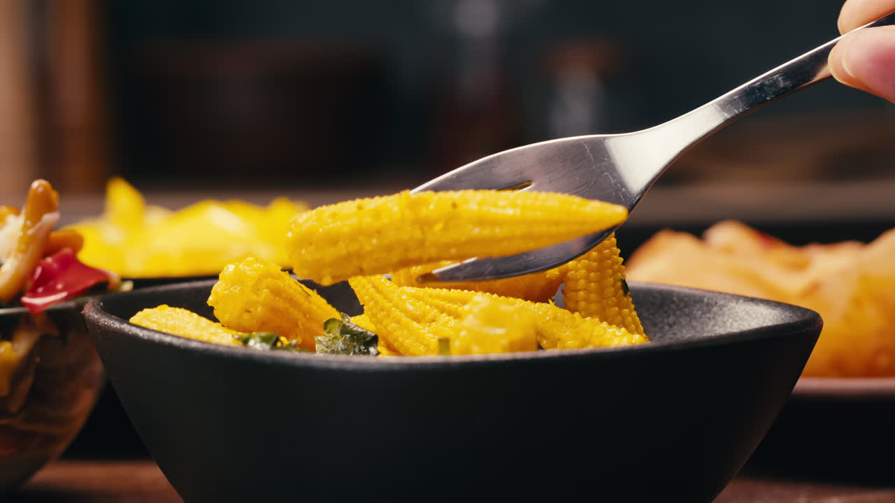 Close-up of fermented yellow mini corn with black pepper on black plate. Preservation of vegetables in glass jars. Fermentation preserved mini corns with spices.