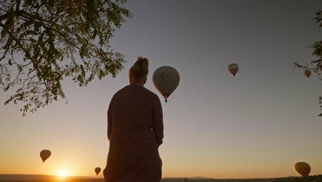 Frauensilhouette-Beobachtet-Romantischen-Sonnenaufgang-Mit-Heißluftballons-Aus-Niedrigem-Winkel