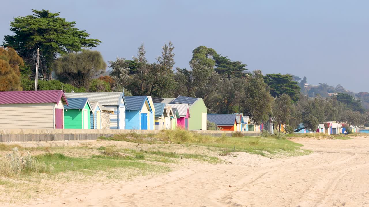 Vibrant beach huts line the sandy shores of Mornington Peninsula under clear skies, captured in a smooth panning shot