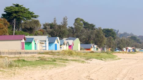 vibrant beach huts line the sandy shores of mornington peninsula under clear skies, captured in a smooth panning shot