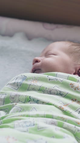 cute newborn baby with closed eyes and fair hair lies in muslin swaddle on baby changing table close view