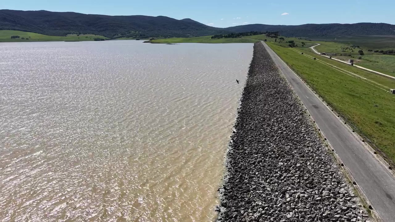 Uma tomada de drone em acompanhamento movendo-se ao longo da barragem de Barbate, mostrando a intersecção da engenharia hidrológica e da cordilheira natural da Andaluzia