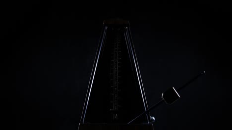 metronome with golden pendulum beats slow rhythm on the dark background