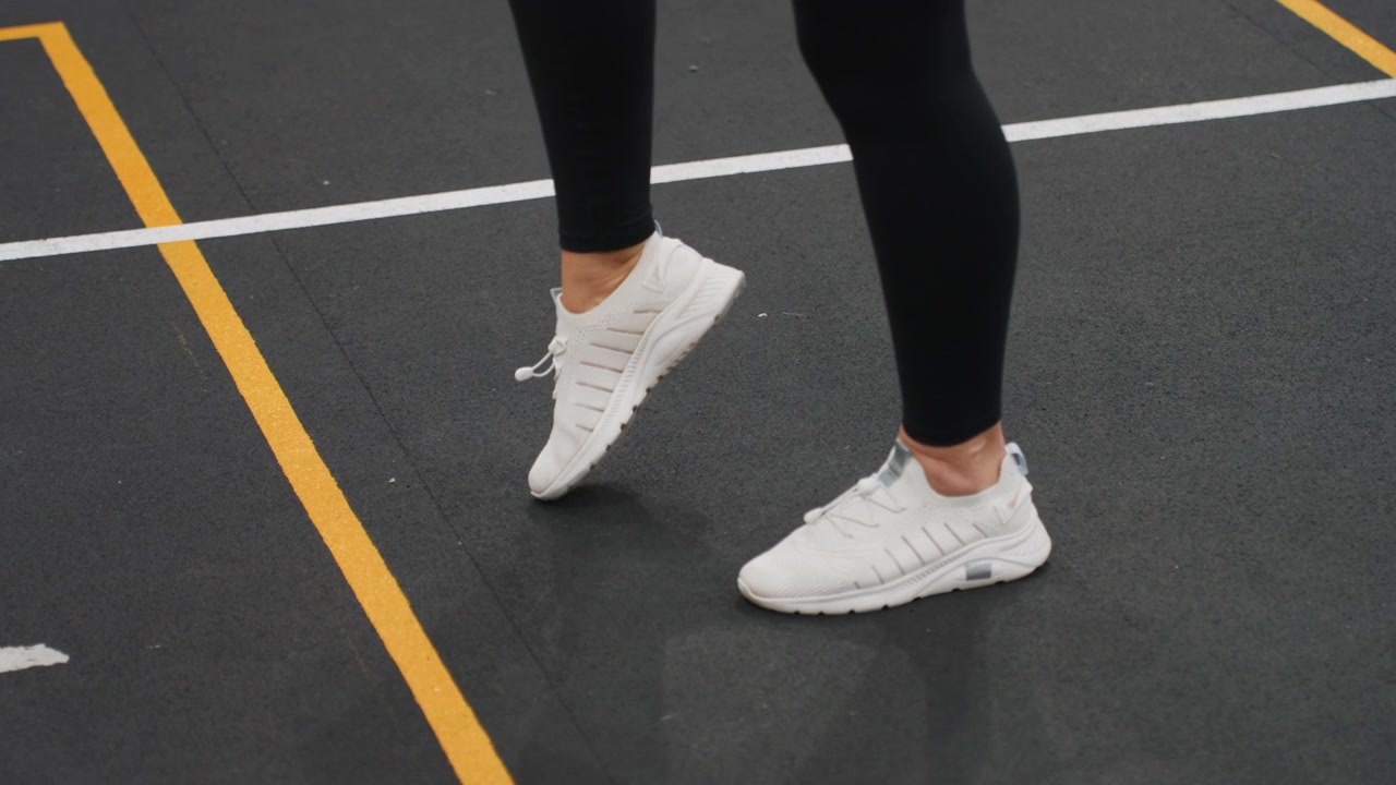 Primo piano dei piedi su un campo da badminton al coperto che eseguono un posizionamento preciso, l'atleta pratica un lavoro misurato di punta e tallone sulle linee segnate, una cadenza lenta e controllata enfatizza tecnica, equilibrio e tempismo.