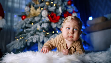 adorable caucasian blond baby lying under the christmas tree. infant child learning to crawl.