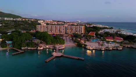 Panoramic-wide-angle-push-in-to-Caribbean-resort-hotel-with-wooden-docks-and-shimering-lights-at-dusk