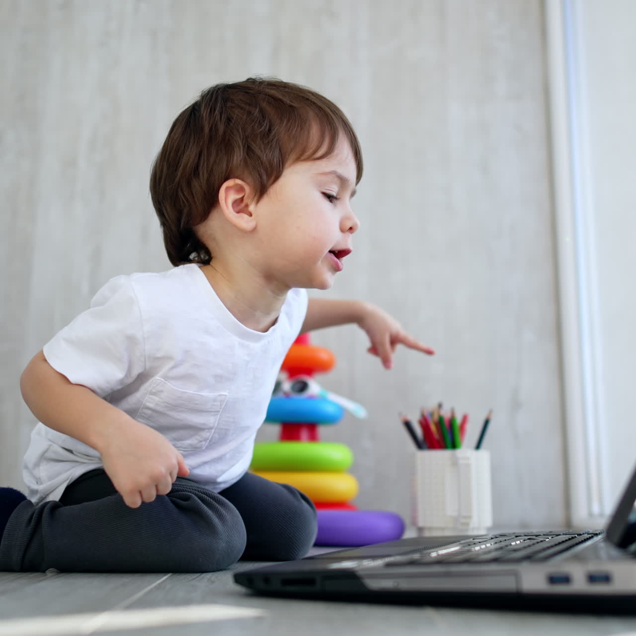 Un adorabile bambino preme il tasto sul laptop e batte le mani allegramente. Il bambino indica lo schermo e chiude il dispositivo. Vista dal basso