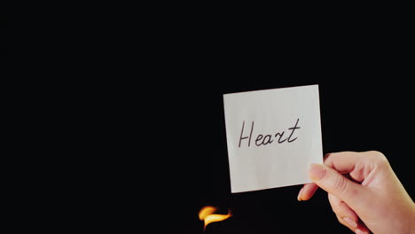 man burns a paper with the inscription heart