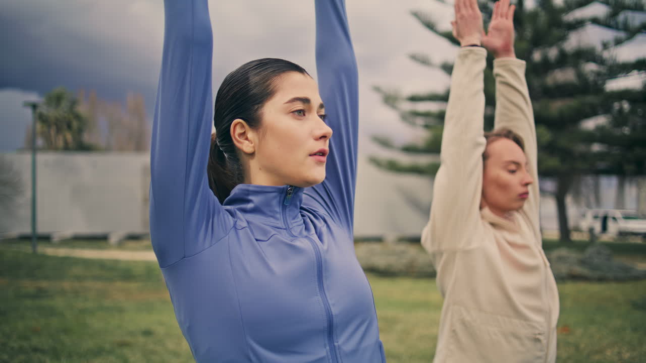 Yogi women raising arms training at park closeup. Ladies making morning yoga