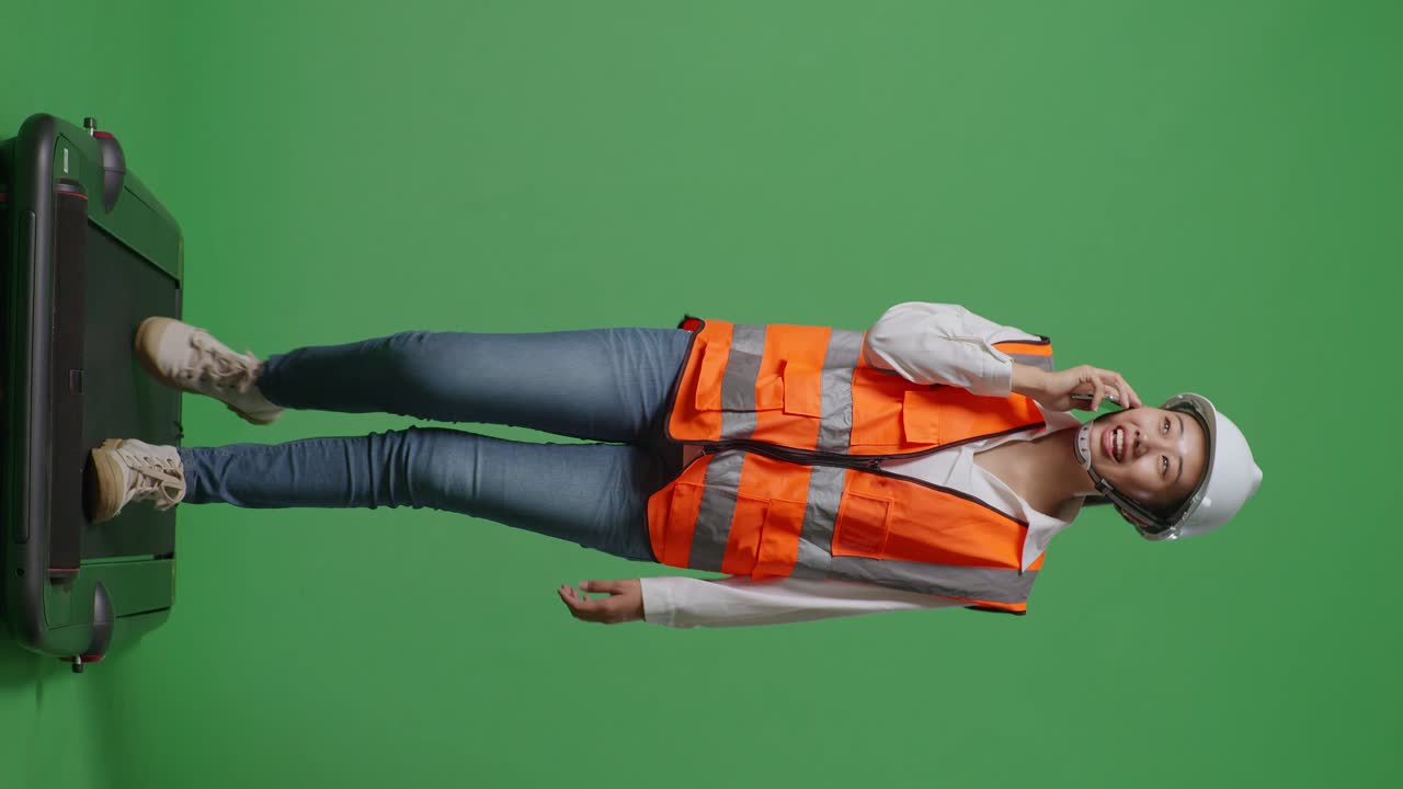 cuerpo lleno de ingeniera asiática con casco de seguridad hablando en teléfono inteligente mientras camina en el estudio de fondo de pantalla verde