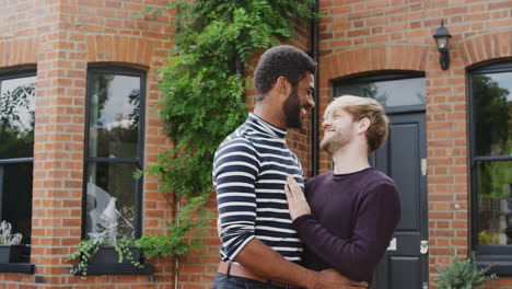 portrait of gay male couple standing outside new home on moving day together kissing