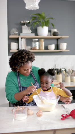 vertical video of african american mother and daughter preparing dough in kitchen, slow motion