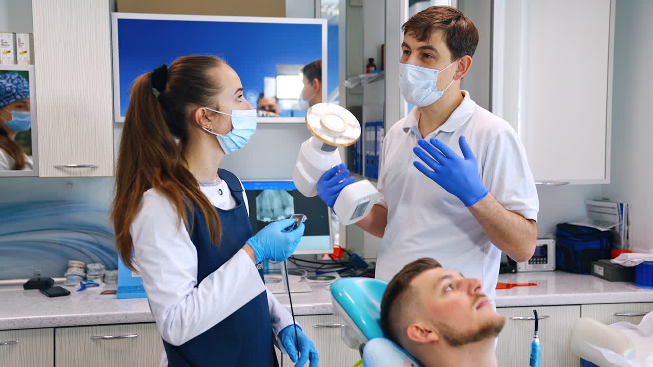 Male teacher in mask and with device in hand talks to a student. Dentistry school practice.