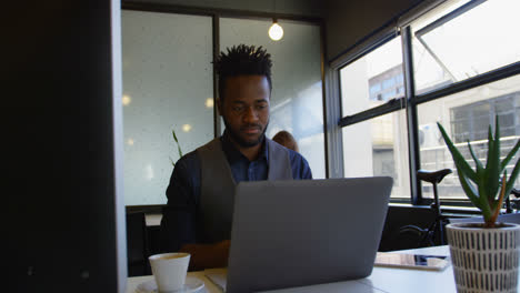 Vorderansicht-Eines-Jungen-Schwarzen-Geschäftsmannes,-Der-Mit-Einer-Tasse-Kaffee-Am-Laptop-Am-Schreibtisch-Sitzt,-4k