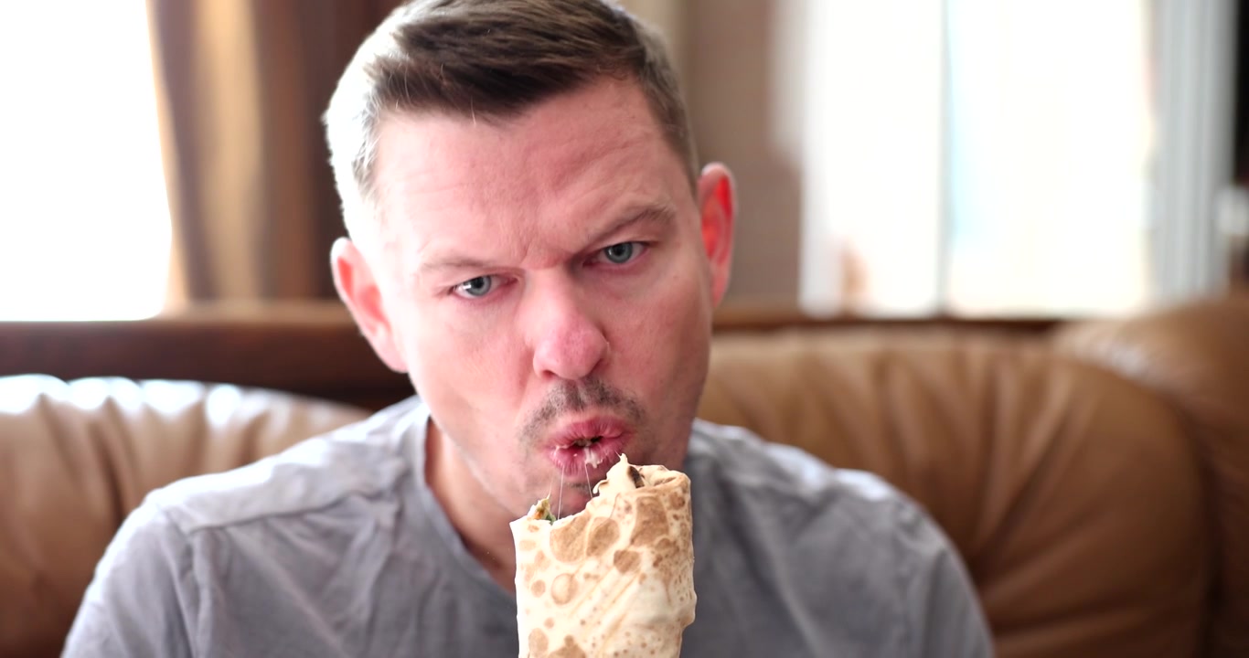 Hombre disfruta de un shawarma con expresión exagerada durante el descanso del trabajo.