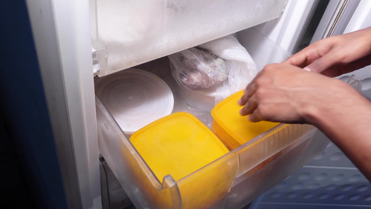 Persona che organizza contenitori per alimenti in un cassetto del congelatore
