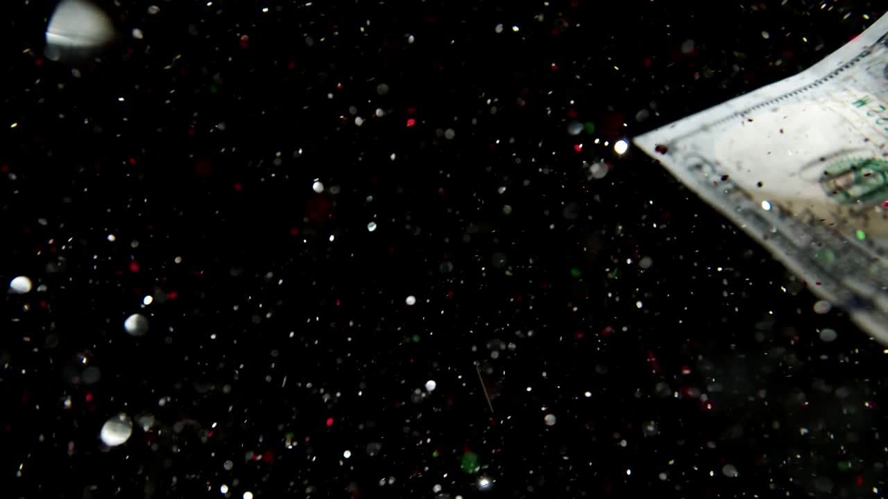 caída volando billetes de dólar estadounidense y volando mezclándose con los brillos brillantes en un fondo negro en 4k loopable. alta calidad caída billetes de dólares en 4k. el video es loopable