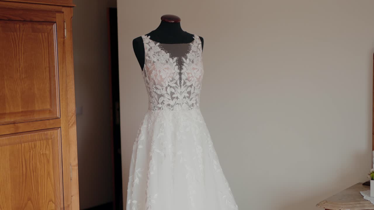 White lace wedding dress with floral details displayed on a mannequin indoors