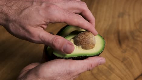 a young man taking the seed out of avocado on wooden table background