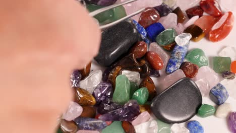 hands use tweezers to sort colorful chakra stones on a white surface under bright lighting