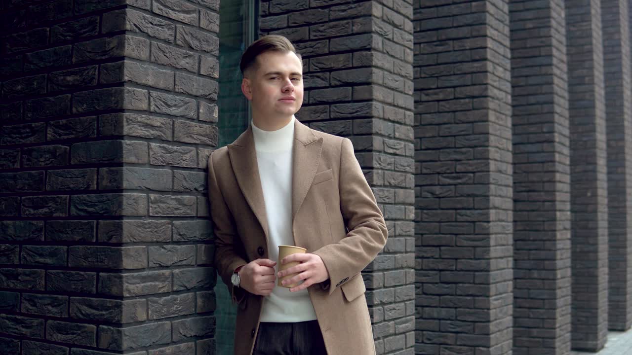 Handsome businessman in brown coat with coffee near the office