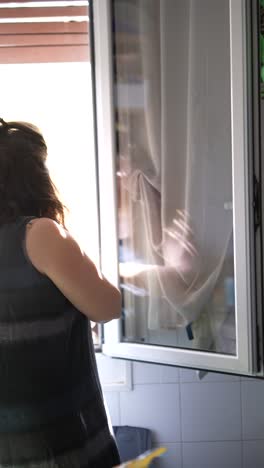 woman in kitchen looking out window and inside cabinet