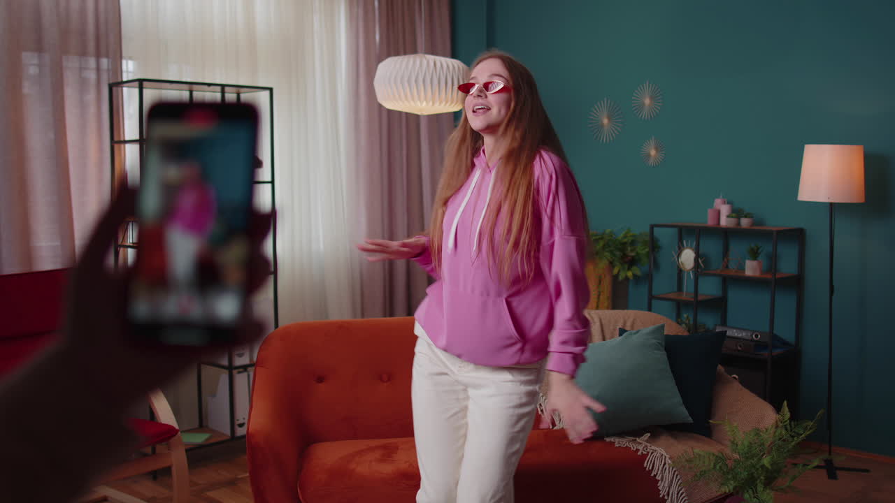 blogger adolescente alegre bailando en la cámara filmando video usando el teléfono móvil en casa en la sala de estar