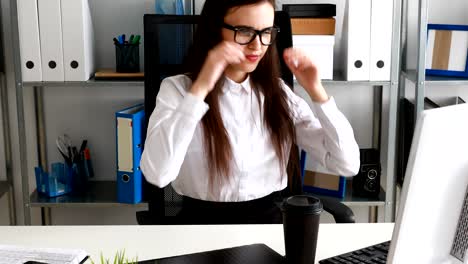 mujer de negocios quitándose las gafas, sosteniendo una taza y sonriendo en una oficina moderna.
