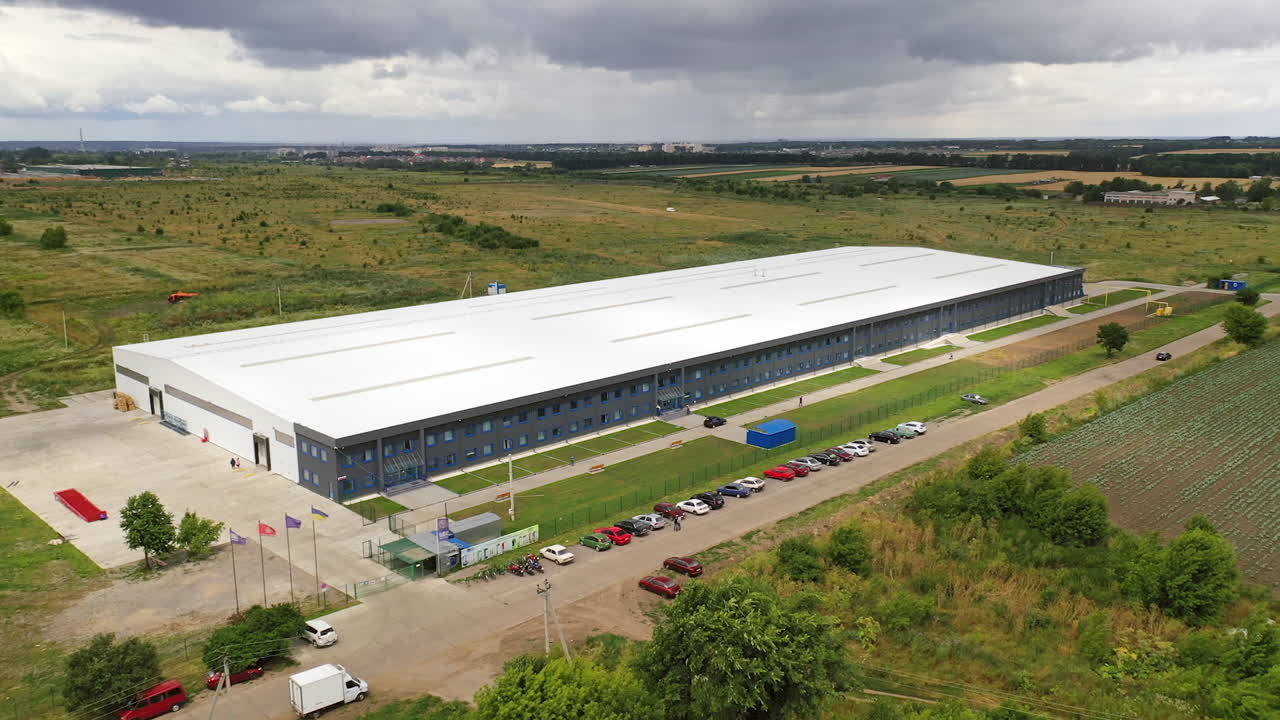Exterior of newly built factory. View from the air on a modern manufacturing construction in the countryside in summer. Aerial view. Motion camera forward.