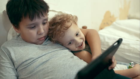 dos hermanos con pad en la cama entretenimiento tableta pc