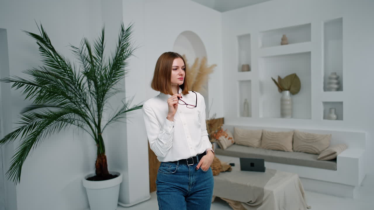 Pensive young man standing in the room holding her glasses. Portrait of female employee in the office.